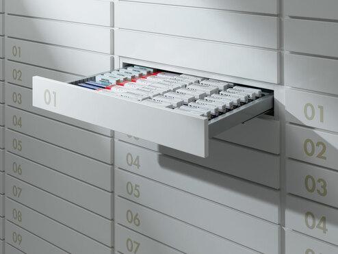 Detailaufnahme von schmalen weißen Medikamentenschubläden mit dezenter Nummerierung und sichtbarer Medikamentenaufteilungen.