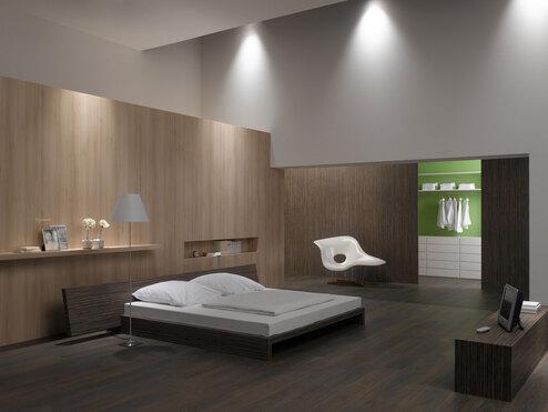 Schlafzimmerimpression von Bett, Nachtisch und Sideboard mit Holzverkleidung an Wand und indirektert Beleuchtung